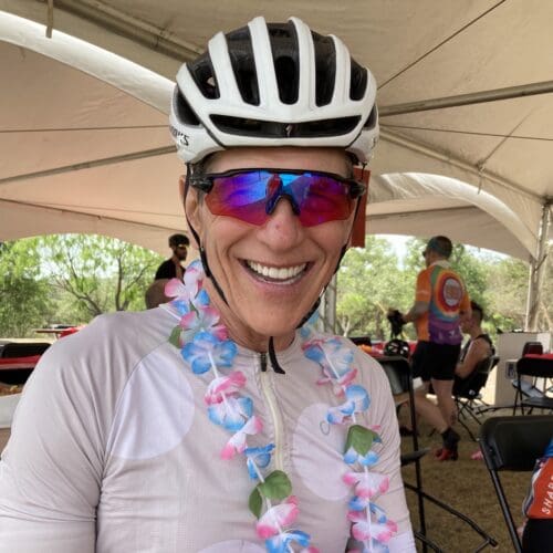 Hill Abell smiling wearing bike hat and a garland of flowers around his neck