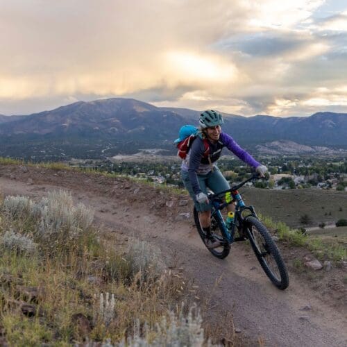 Anna Ulrich riding her mountainbike on a trail with the mountains behind her