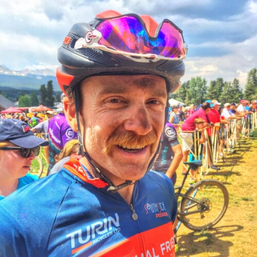 Tom Wagner at a mountainbiking race with his racing shirt on and colorful sunglasses on his helmet